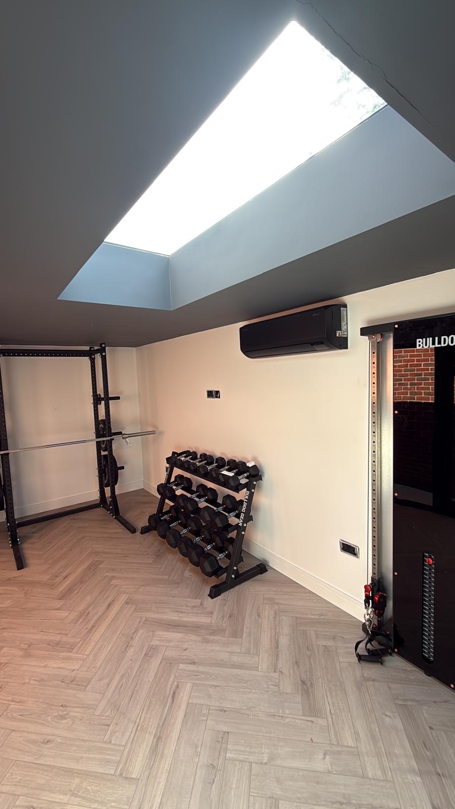 Black air conditioning unit installed in a modern home gym with skylight