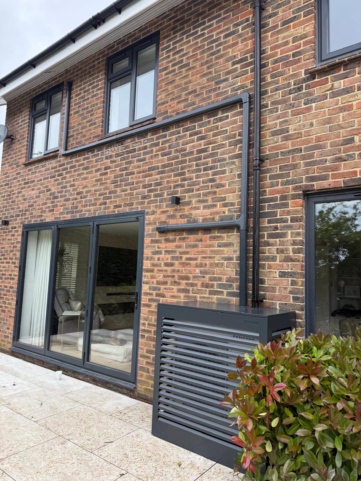 Outdoor air conditioning unit housed in a modern slatted enclosure beside a brick home