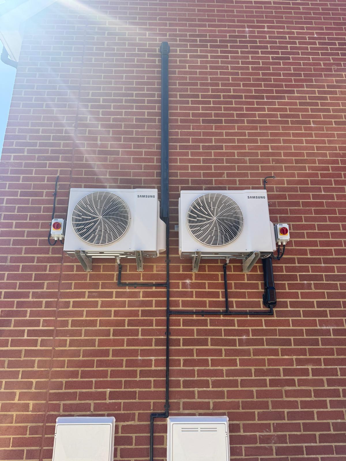 Two Samsung outdoor air conditioning units mounted on a brick wall