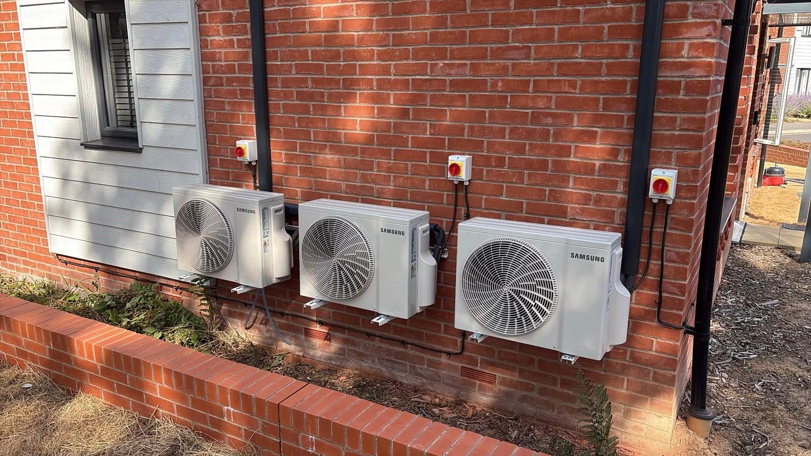 Three Samsung outdoor air conditioning units mounted on a brick wall