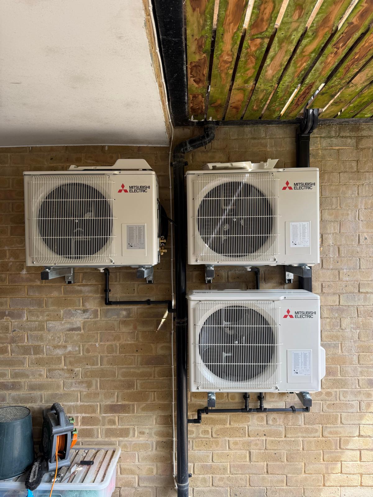 Three Mitsubishi Electric outdoor air conditioning units mounted on a brick wall